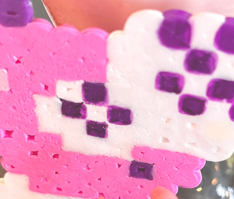a photo of a perler bead creation of pim sitting upright against a parfait in a clear glass. the person holding the camera points a strawberry pocky stick towards the pim's mouth, making it look like he's being fed.